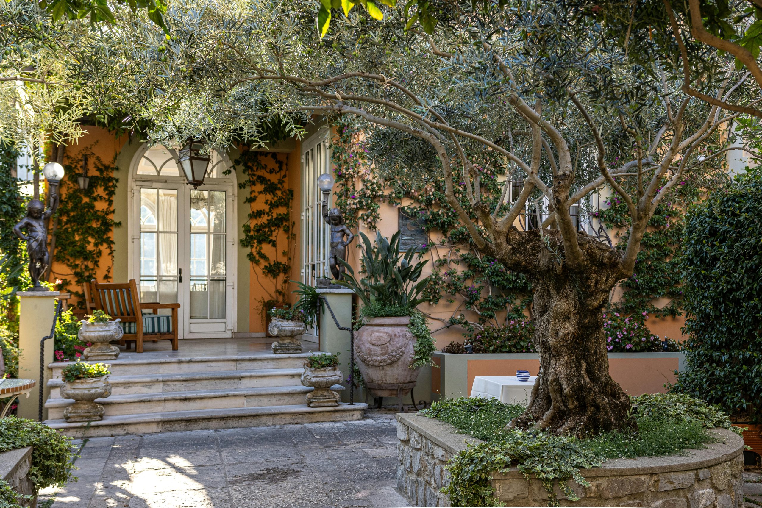 Elegant Mediterranean villa entrance with lush greenery and classic decor.
